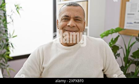 Porträt eines selbstbewussten hispanischen Mannes mittleren Alters, der in einer modernen Büroumgebung lächelt. Stockfoto