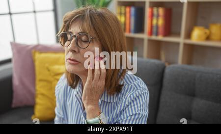 Reife Frau, die Zahnschmerzen hat, während sie drinnen auf der Couch sitzt. Stockfoto