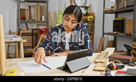 Eine junge südasiatische Frau arbeitet intensiv in einer Tischlerei, umgeben von Werkzeugen und Holz. Stockfoto