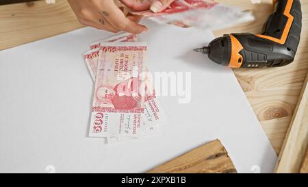 Frau, die isländische Krone in einer Tischlerei hält, mit einem Bohrer auf einem Holztisch. Stockfoto