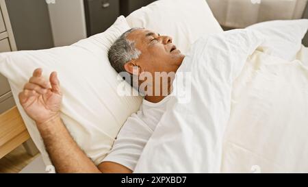 Ein reifer Mann schläft friedlich in einem weißen Bett drinnen und bietet Entspannung und Erholung zu Hause. Stockfoto