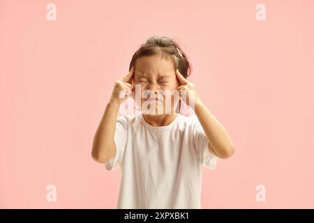 Fünf Jahre altes japanisches Mädchen konzentriert sich mit geschlossenen Augen und Fingern auf Tempel steht über rosa isoliert Stockfoto