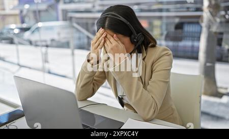 Gestresste junge Frau mit Headset-Blick auf den Laptop in einem hellen Büro Stockfoto
