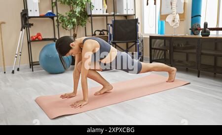 Hispanische Frau, die in einer Rehabilitationsklinik mit physiotherapeutischen Geräten im Hintergrund trainiert. Stockfoto