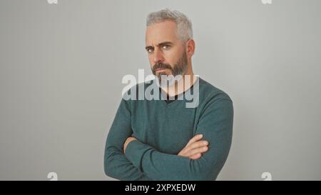 Ein ernsthaft aussehender kaukasier mit Salz-Pfeffer-Bart, lässigem Pullover, posiert mit überkreuzten Armen vor weißem Hintergrund. Stockfoto