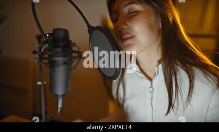 Junge Frau singt drinnen an einem Mikrofon in einem Aufnahmestudio, porträtiert Musik, Aufführung und Unterhaltung. Stockfoto