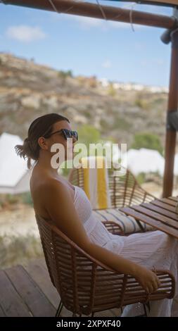 Eine junge hispanische Frau entspannt sich draußen auf einem Campingplatz in afrika, sitzt auf einem Korbstuhl in einem Zelt und genießt das warme Wetter und die natürliche Surro Stockfoto