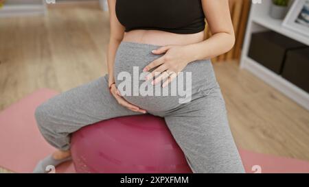 Schwangere hispanische Frau übt pränatalen Yoga auf einem Ball drinnen. Stockfoto