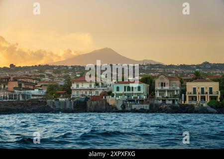 Malerischer Blick auf Catanias farbenfrohe Gebäude am Wasser mit dem Vulkan Ätna im Hintergrund, von einem Boot bei Sonnenuntergang erfasst. Sizilianische coasta Stockfoto