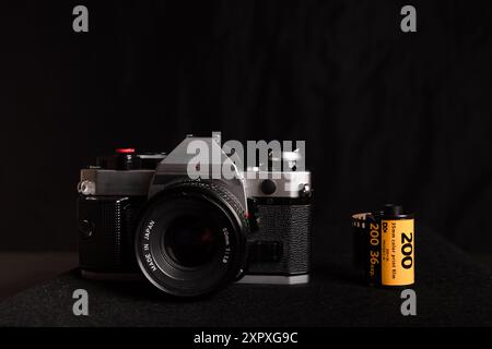 Detaillierte Ansicht einer alten Kamera mit einer Rolle 35-mm-Film auf schwarzem Hintergrund, die traditionelle Fotoausrüstung darstellt. Stockfoto