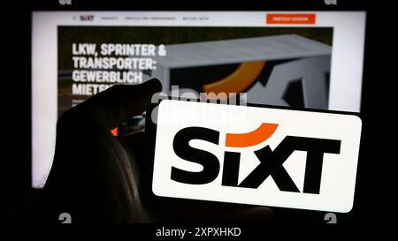 Person mit Smartphone und Logo der deutschen Autovermietung Sixt SE vor der Website. Schwerpunkt auf dem Display des Telefons. Stockfoto