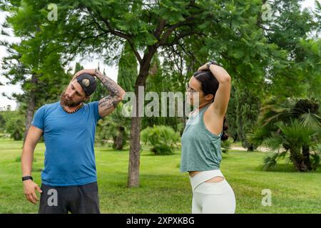 Ein junger rotbärtiger Mann und eine junge Frau konzentrieren sich darauf, gemeinsam den Hals in einem Park zu Strecken. Ein paar Workouts, Stretching-Routinen und ein Stockfoto