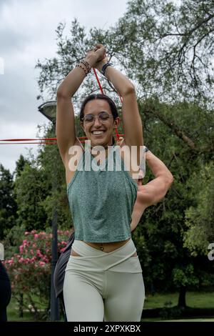 Eine junge Frau trainiert im Freien mit Widerstandsbändern, lächelt, während sie ihre Trainingsroutine in einer natürlichen Umgebung durchführt, um Gesundheit, Fitness, Stockfoto