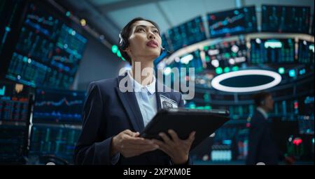 Junge weibliche Börsenmaklerin, die an einem Tablet-Computer mit Echtzeit-Aktien, Rohstoffen und Börsenmärkten arbeitet. Professioneller asiatischer Investmentagent in einem modernen Bürogebäude. Stockfoto