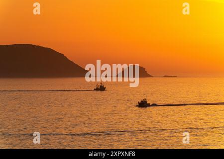 Zwei Fischerboote segeln bei Sonnenuntergang im Ría de Pontevedra in Galicien in der Abenddämmerung mit den ruhigen Ons-Inseln im Hintergrund. Stockfoto