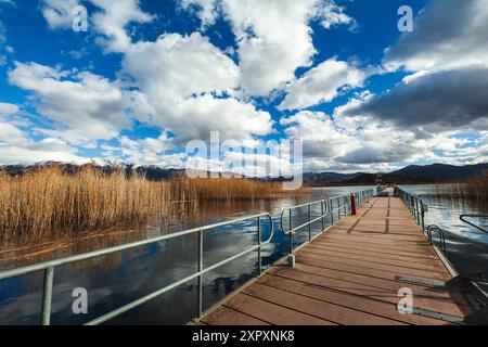 Die schwimmende, hölzerne Brücke zur Insel Agios Achillios, im kleinen Prespa-See, Griechenland, an einem kühlen Wintertag mit einem Himmel aus erstaunlichen weißen Wolken Stockfoto