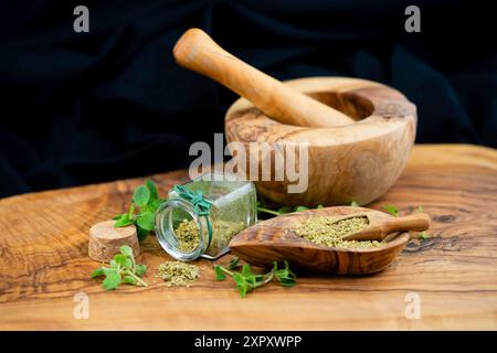 Wildes Origanum, wildes Marjoram (Origanum vulgare), frischer Oregano, gerieben in einem Glas und auf Holzschale, mit Mörtel Stockfoto