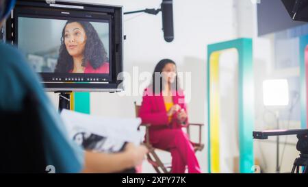 Lebendiges Bild Einer jungen schwarzen Gastgeberin in Einem rosafarbenen Anzug, das während Einer TV-Show eine lebhafte Diskussion führt, umgeben von moderner Videografieausrüstung und farbenfrohem Set-Design. Stockfoto