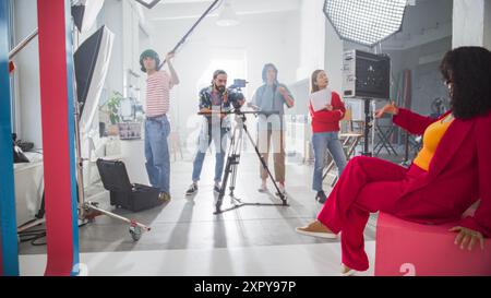 Diverse Team engagierte sich an Einem kreativen Filmdreh in Einem Bright Studio mit Einer weiblichen Regisseurin, Einem männlichen Kameramann und Assistenten, die sich auf Produktionsaufgaben, Teamwork und Innovation konzentrieren. Stockfoto