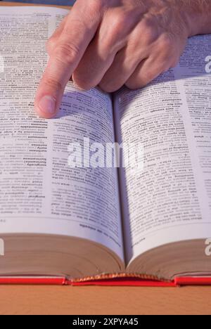 Die Hand eines Mannes, der ein Wort im Wörterbuch aufsucht. Ansicht schließen. Stockfoto