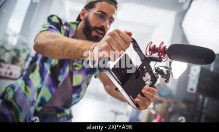 Junger männlicher Kaukasischer Filmemacher, der Eine moderne Kamera mit Mikrofon in Einem Studio betreibt, Inhalte für Ein kreatives Werbeprojekt aufnimmt, Teamwork und professionelle Ausrüstung präsentiert. Stockfoto