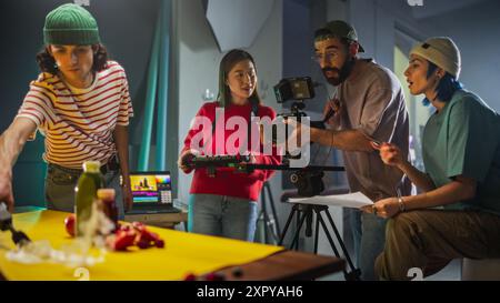 Die Dynamic Young Film Crew führte Eine lebhafte Diskussion über Ein buntes Set mit Einer asiatischen Kameramann, die Eine Kamera anpasst, während ihr diverses Team an Einem kreativen Videoproduktionsprojekt mitarbeitet Stockfoto