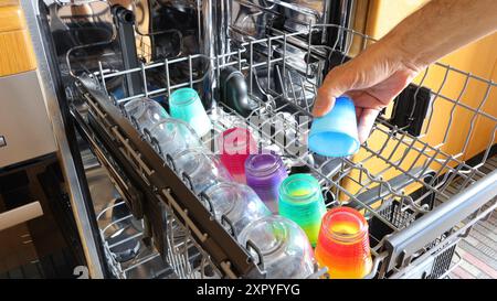 Geschirrspüler mit Glasgläsern und kleinen farbigen Tassen, im Vordergrund auf dem Regal, mit der Hand eines Mannes. Stockfoto