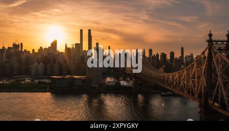 Hubschrauberfoto über Ed Koch Queensboro Bridge mit Manhattan Wolkenkratzern. Wunderschöne Abendsonne, die mit warmem Sonnenuntergangslicht leuchtet. Foto mit Fokus auf Upper East Side Gebäude Stockfoto