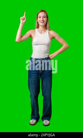 Eine junge Frau in weißem Tanktop und Jeans zeigt sich gegen Green Screen Stockfoto
