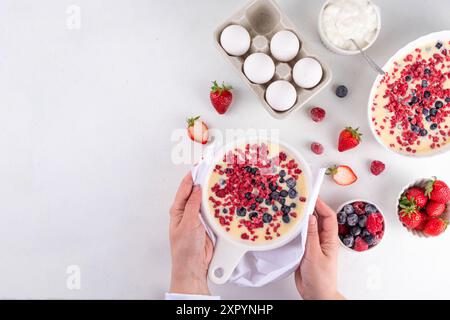 Kochen Herstellung von gebackenem Joghurt gesundes Dessert. Frau Hand kochen Ofen gebacken griechischer Joghurt Dessert mit frischen gefrorenen Beeren, auf weißem Küchentisch, mit Stockfoto