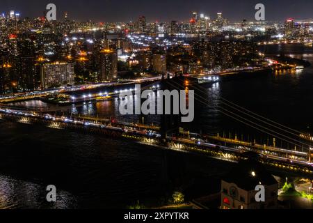 Luftbild der Skyline von New York City von einem Hubschrauber bei Nacht. Berühmte Wolkenkratzer-Gebäude mit Manhattan Bridge. Geschäftiges, vielfältiges Megapolis mit Autos, Booten und Menschen, die sich bewegen Stockfoto