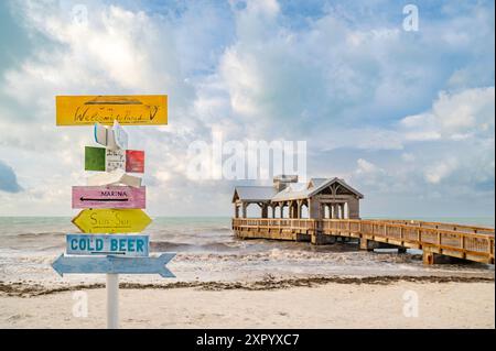 Ein farbenfroher hölzerner Wegweiser an einem Strand mit einem Holzsteg im Hintergrund. Stockfoto