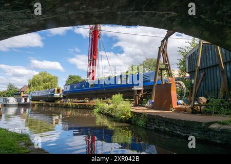 Altes Schmalboot, das von einem Kran aus dem Kanal in einen Bootswerft gehoben wird, um Reparaturen von unterhalb des Bogens einer benachbarten Brücke aus zu machen. Stockfoto