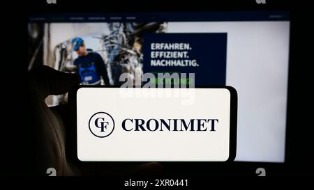 Person, die ein Mobiltelefon mit dem Logo des deutschen Metallrecyclingunternehmens Cronimet Holding GmbH vor der Business-Website hält. Schwerpunkt auf dem Display des Telefons. Stockfoto