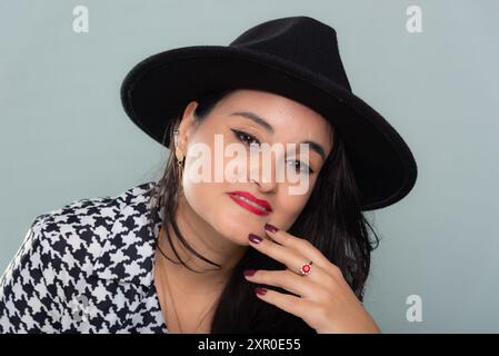 Nahporträt einer schönen kaukasischen Frau mit schwarzem Hut und schwarz-weißem Outfit. Isoliert auf hellgrünem Hintergrund. Stockfoto