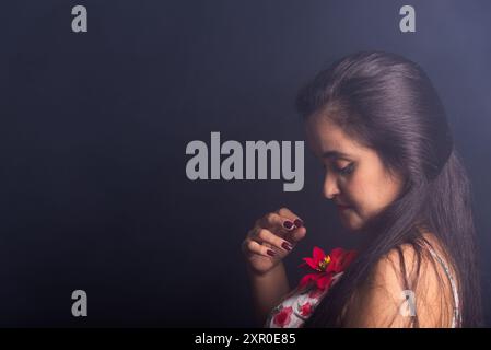 Schwarzhaarige Frau mit einer roten Blume auf dem linken Ohr posiert für das Foto. Isoliert auf farbenfrohen rauchigen Hintergrund. Stockfoto