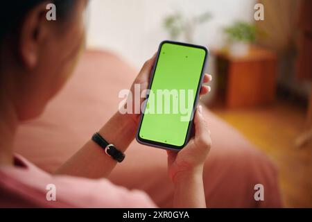 Smartphone mit grünem Bildschirm in gemütlichem Schlafzimmer Stockfoto