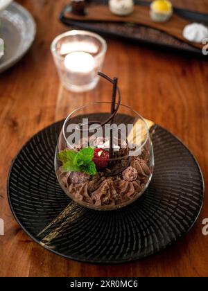 Eine Nahaufnahme eines Gourmet-Schokoladen-Desserts garniert mit Minze und Himbeere, serviert in einem Glas auf einem Holztisch. Vertikale Aufnahme. Stockfoto