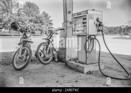 Mazedonien, Arkansas, USA – 23. Juni 2024: Horizontale Aufnahme von zwei Oldtimer-Motorrädern neben einer alten Mobil-Gaspumpe im Jahr 1975. Stockfoto