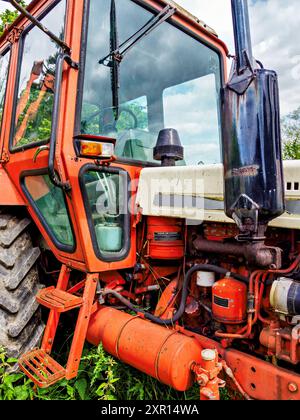 Nahaufnahme eines roten Vintage-Traktors auf dem Feld mit komplexen Motordetails und robustem Design. Stockfoto