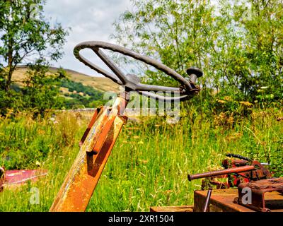 Nahaufnahme eines rostigen Traktorlenkrads auf einem bewachsenen Feld mit landschaftlicher Kulisse. Stockfoto