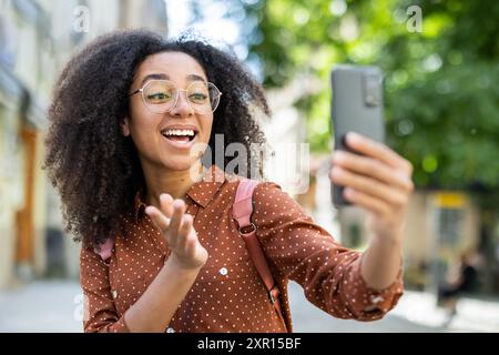 Fröhliche Touristin, die an einem sonnigen Tag durch die Stadt spaziert und ihr Telefon für einen Videoanruf hält. Sie genießt ihren Urlaub, Sightseeing und verbindet sich mit Freunden. Stockfoto