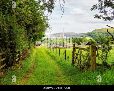 Ein ruhiger Landweg in einer üppigen, grünen Landschaft mit fernen Hügeln und Industriekohnen am Horizont. Stockfoto