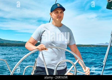 Ein See umgeben von felsigen Bergen und Wäldern. Junger Mann auf dem See am Steuer einer Yacht Stockfoto