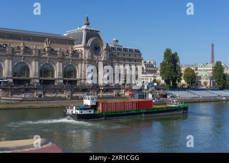 Paris, Frankreich, 08.08.2024 Frachtschiff auf der seine vorbei am Musée d’Orsay (Museum von Orsay), im Hintergrund der Eiffelturm Stockfoto