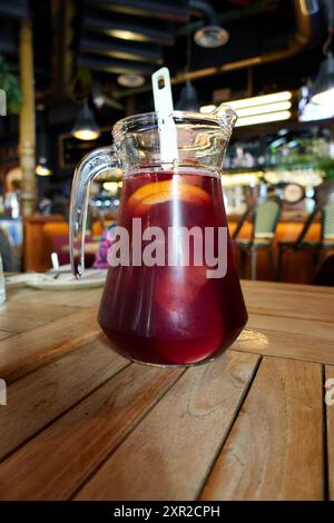 Glaskanne mit Sangria, typisches Cocktailgetränk aus Spanien mit Rotwein, Früchten und Limonade oder Orangen- oder Zitronensoda, auf einem Holztisch in einem Restaurant Stockfoto