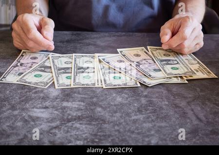 Hände und Dollarscheine, eins, fünf und zehn, verteilt auf einem strukturierten Tisch Stockfoto