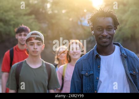 Schwarzer Mann aus Senegal im Vordergrund, der eine multirassische Gruppe junger Menschen anführt - Millennial Friends Walking in the Park - Selective Focus Stockfoto