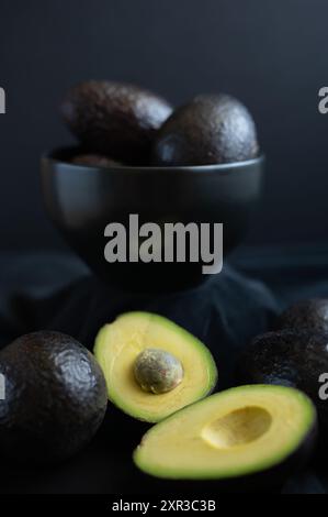 Vertikales Bild einer geschnittenen Avocado vor einer schwarzen Schüssel. Stockfoto