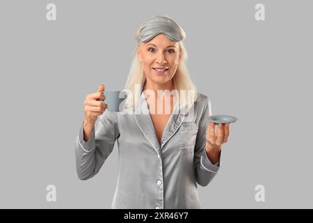 Reife Frau im Pyjama mit einer Tasse Kaffee auf grauem Hintergrund Stockfoto